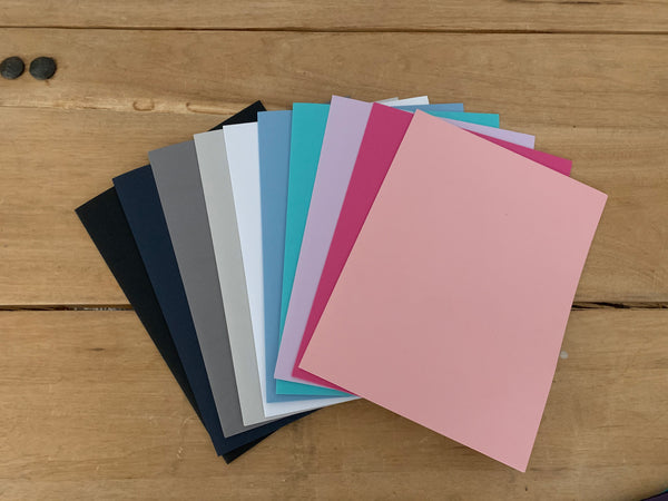 Pocket Folders from left to right in Black, Night, Pewter, Fog, White, Bluebell, Tiffany, Plum, Peony, and Blossom